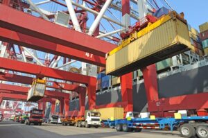 Blog cost of shipping: Image shows TEUs being unloaded from a ship and loaded onto chassis for truck transport
