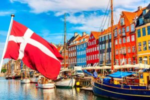 Blog Political development: Picture of Danish flag in front of a number of boats in front of a number of brightly colored row houses
