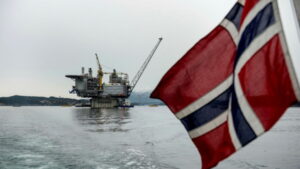 Blog Political development: An image of a Norwegian flag in the foreground with an ocean oil platform in the background