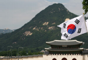 Blog Economic value: Picture of the flag of South (the Republic of) Korea with a building and hill in the background,