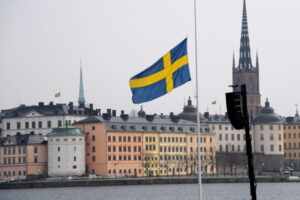 Blog Political development: An image of the Swedish flag in front of a limestone coloured building