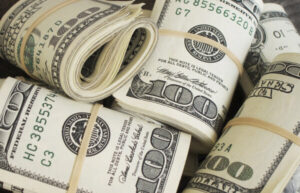 Blog What causes inflation: Image shows a bunch of rolls of USD hundred dollar bills